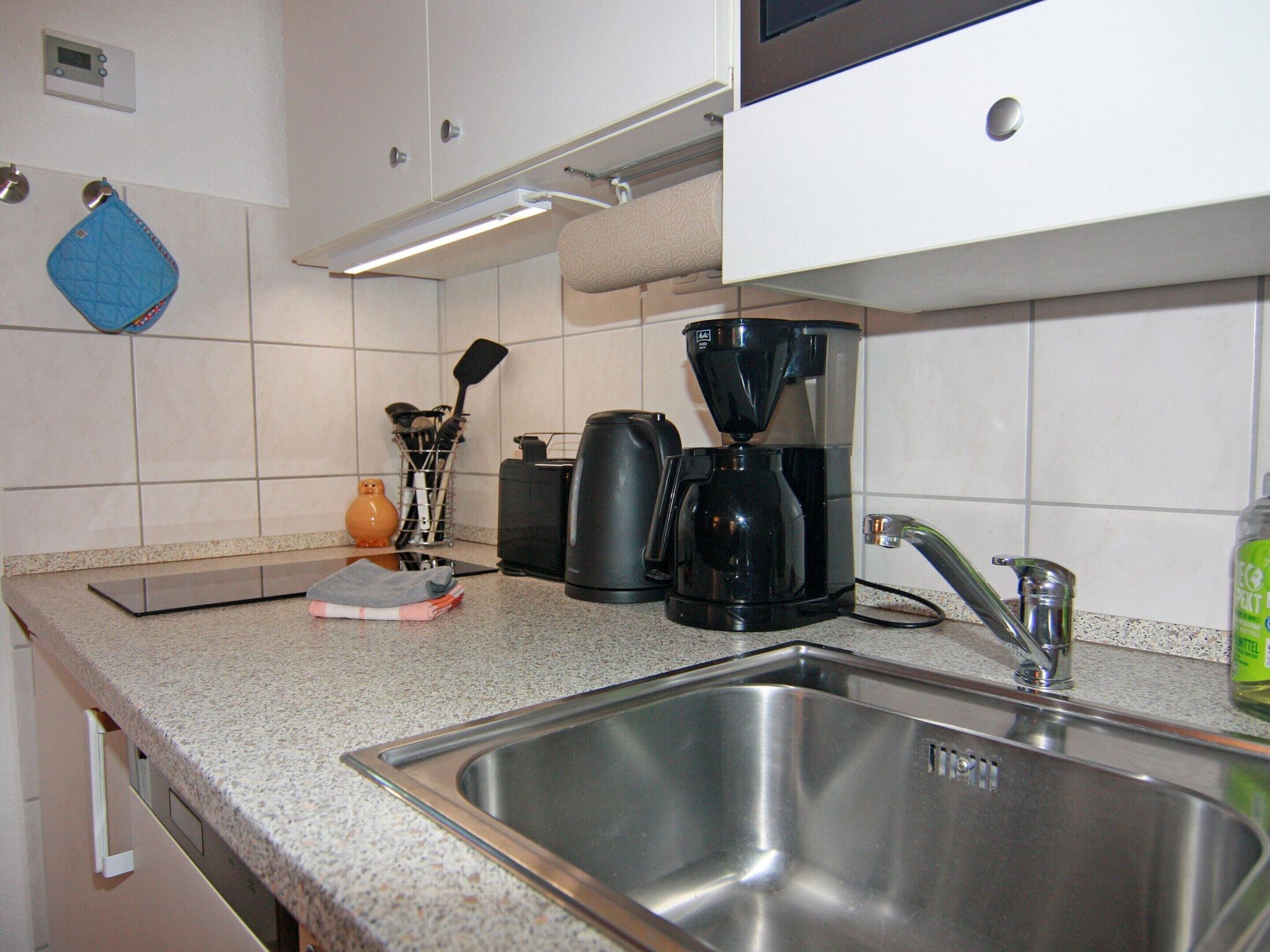 Una cucina con lavello in acciaio inox, una macchina da caffè e un bollitore.