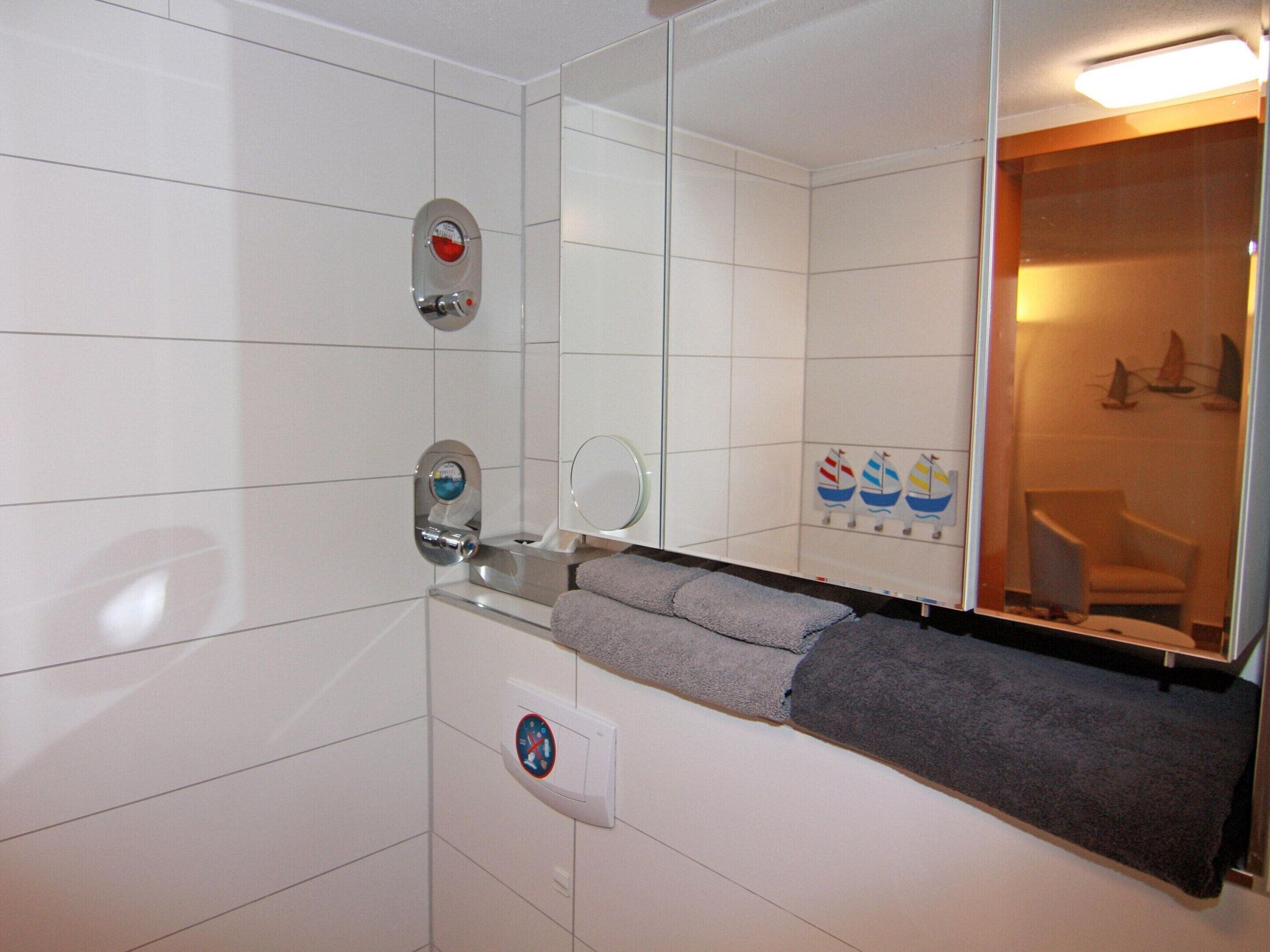 A bathroom with white tiles, a towel rack, a mirror, and a shower area.