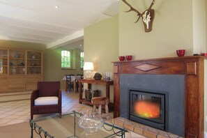A living room with a fireplace, a chair, a table with glassware, and a wooden cabinet.
