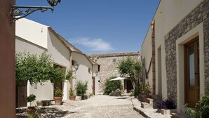 A narrow cobblestone street flanked by buildings with stone walls and tiled roofs, potted plants, and a street lamp. - Holiday Home in Buseto Near San Vito Lo Capo (Buseto Palizzolo)