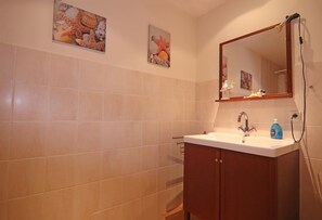 Um banheiro com azulejos bege, um armário de madeira, uma pia com espelho e duas obras de arte de estrelas-do-mar fixadas na parede.
