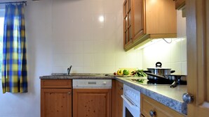 Ett kök med träskåp, diskmaskin, ugn och en bänkskiva med en kastrull och grönsaker på.