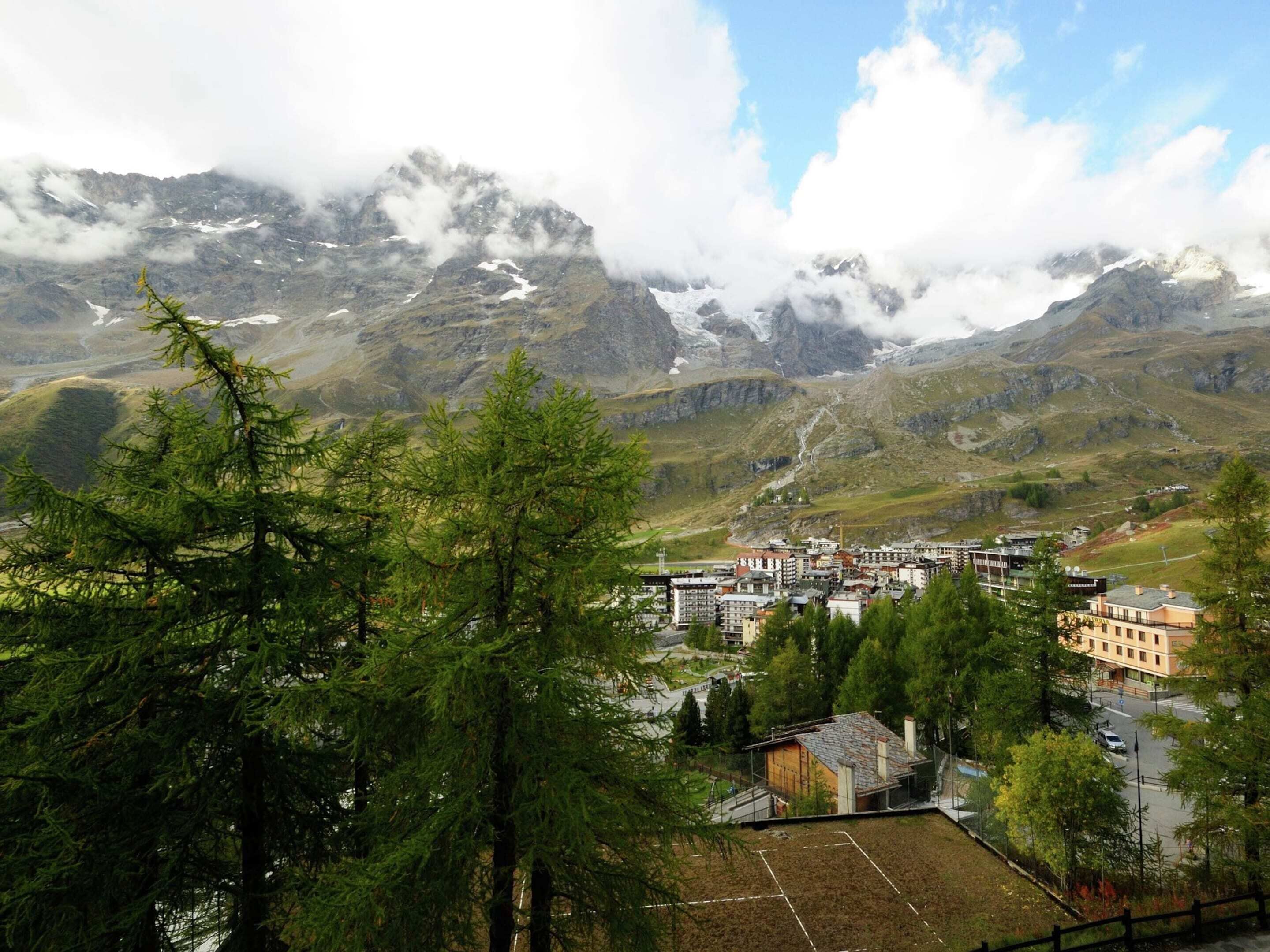 Un pueblo montañoso con edificios rodeados de árboles y picos nevados.