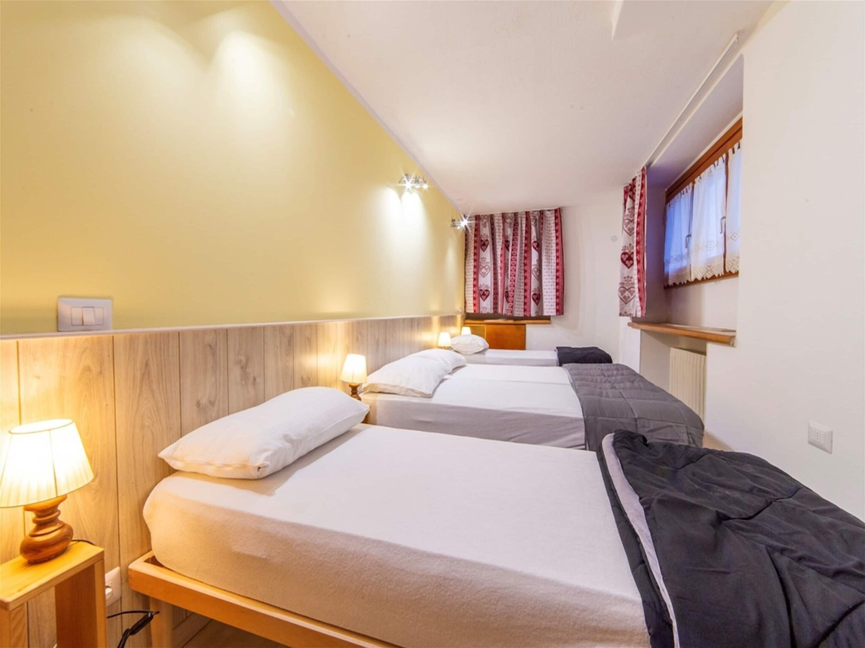 A hotel room with two beds, a wooden headboard, a nightstand with a lamp, and a window with curtains.