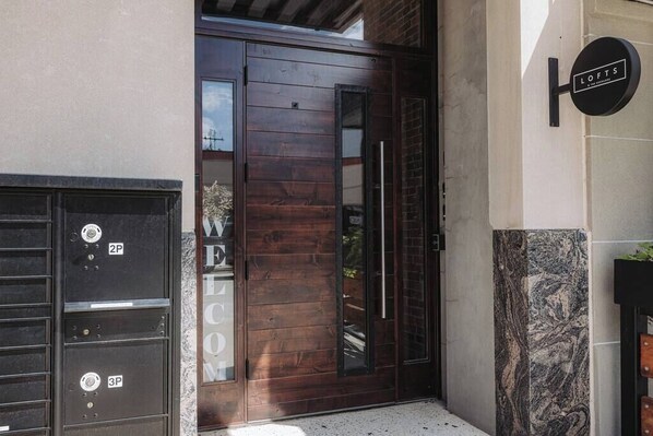 Entrada de un edificio moderno con puerta de madera, un portón negro y un letrero que dice "LOFTS".