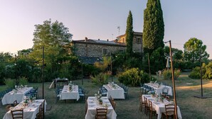 An outdoor dining area with multiple tables set for a meal, surrounded by greenery and a stone building in the background. - Adorable Farmhouse in Asciano (Asciano)