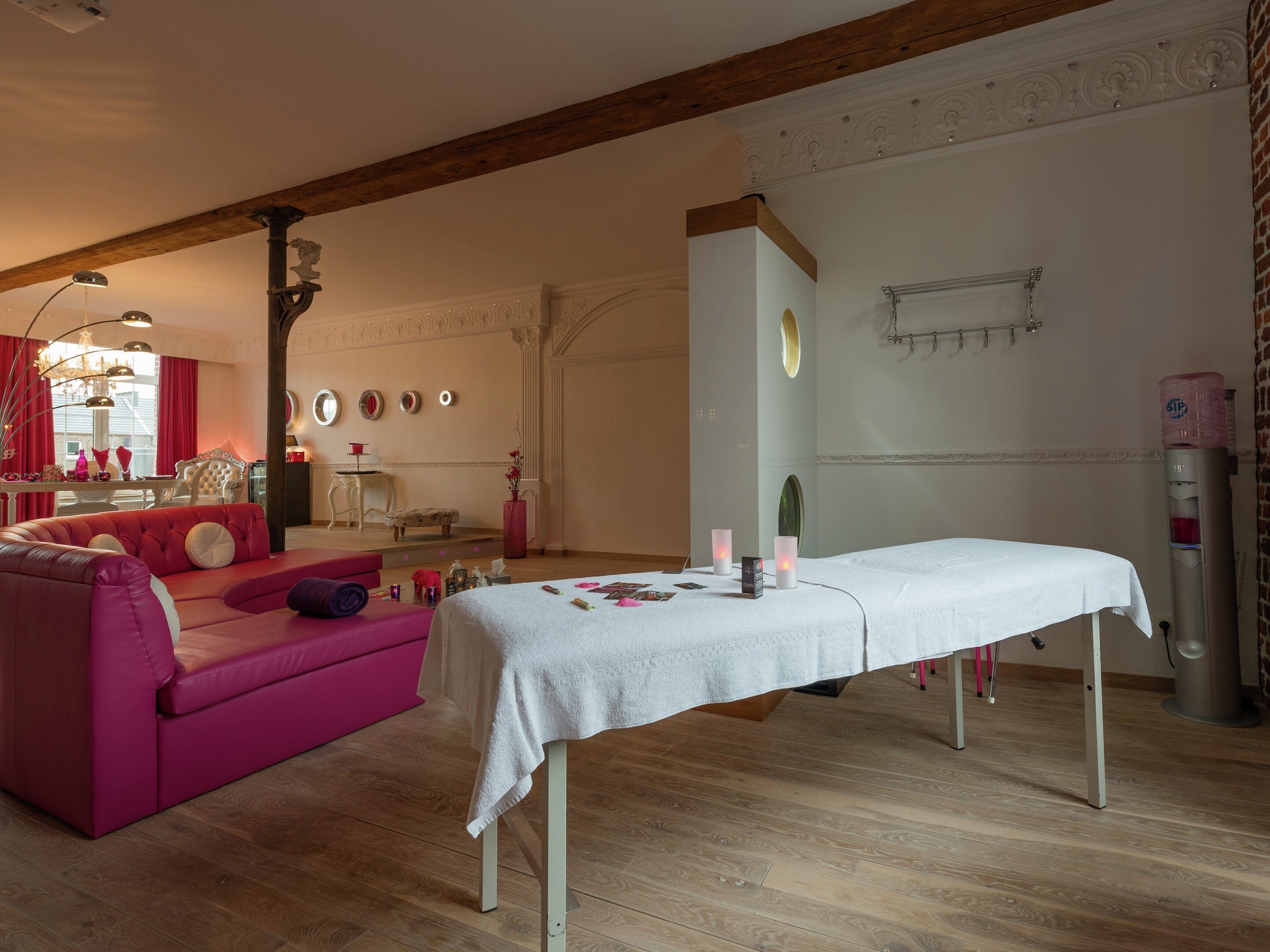 Une pièce comprenant une table de massage, un canapé rose et un coin repas agrémenté d’un lustre.