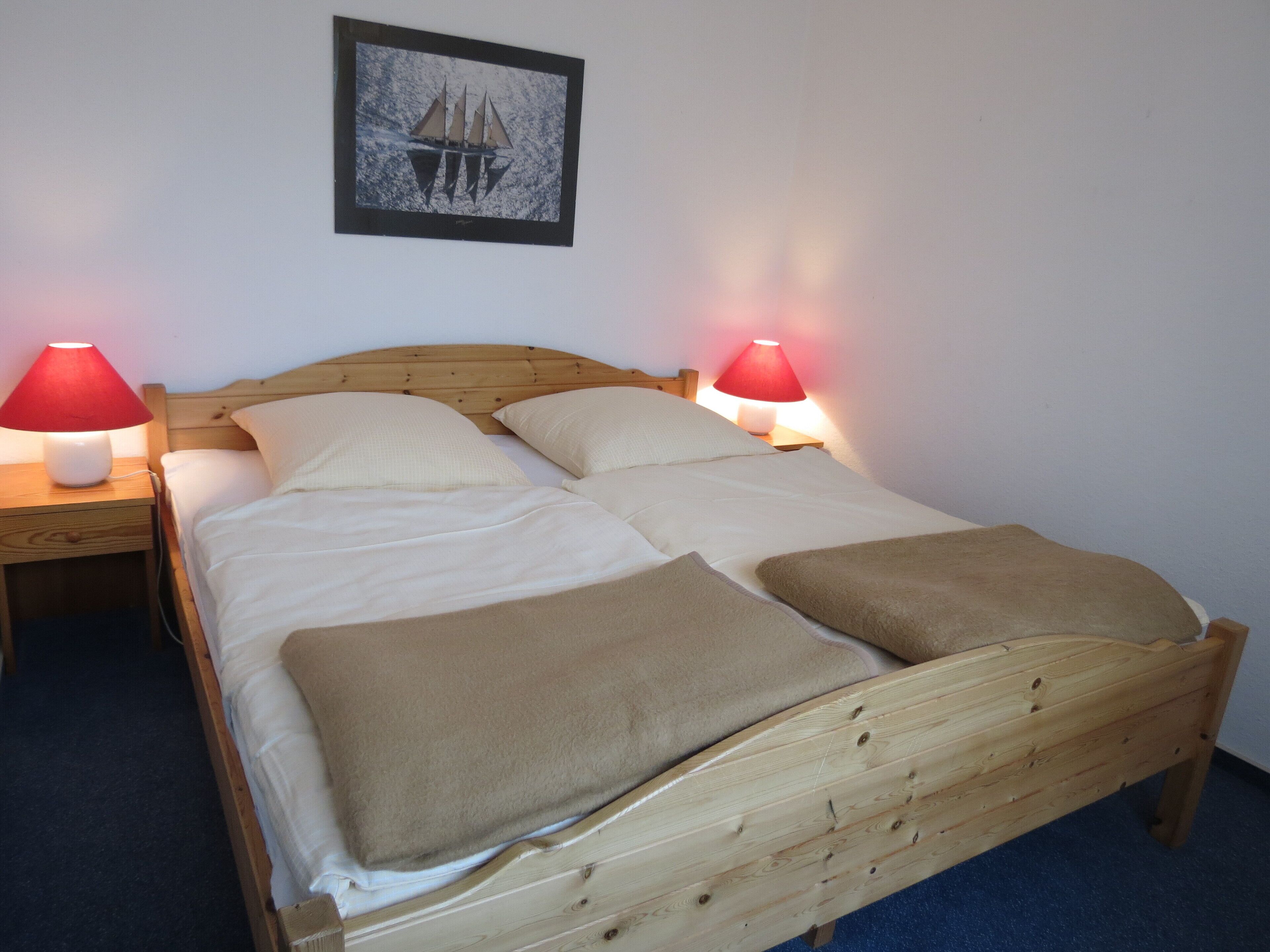 Een bed met houten frame, twee nachtkastjes en twee rode lampen.
