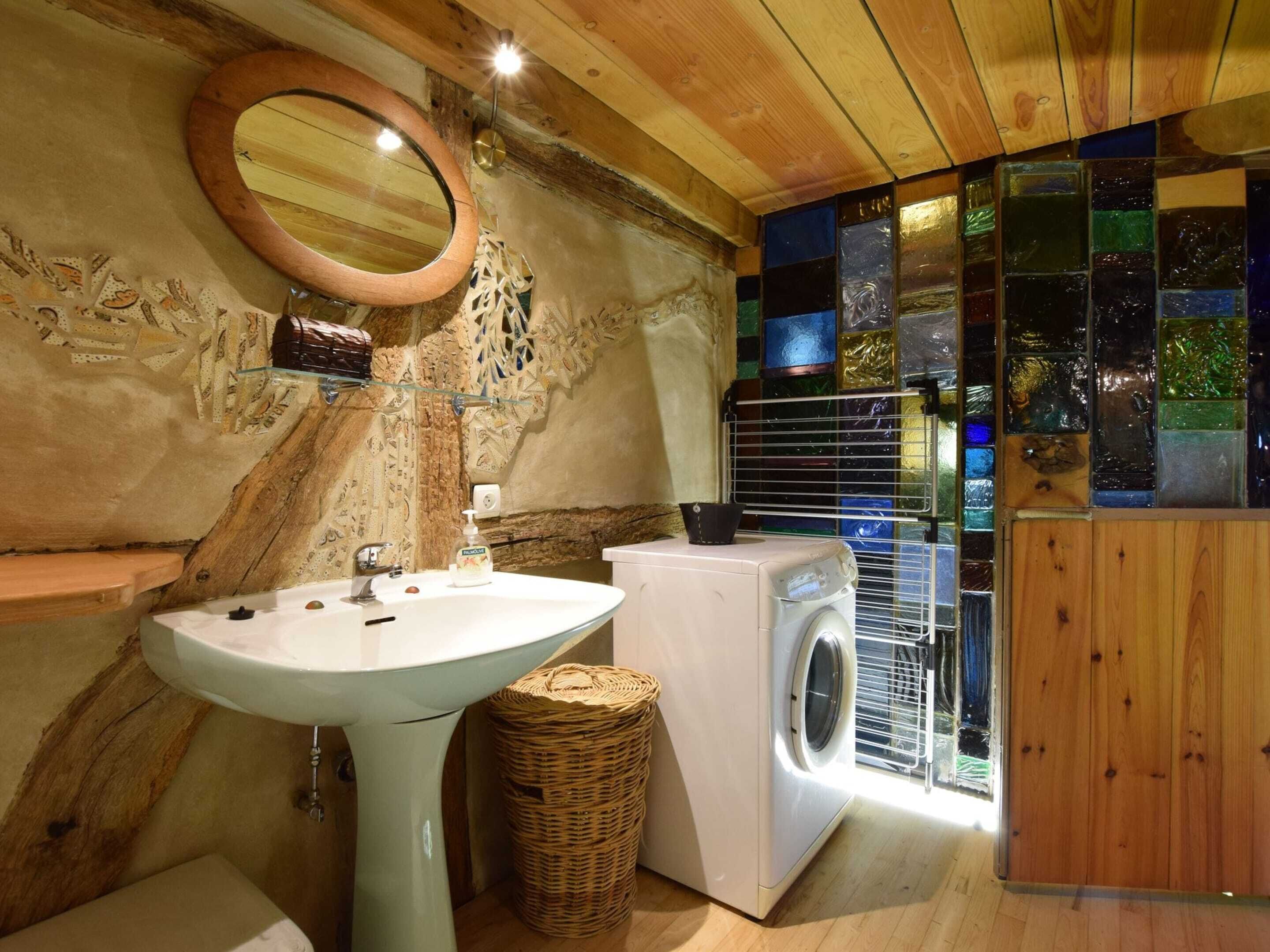 A compact bathroom with a sink, washing machine, and a mirror.
