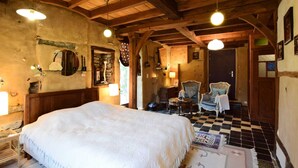 A rustic bedroom with a large bed, wooden beams, and a checkered floor. - Holiday Home in Longueville (Durbuy)