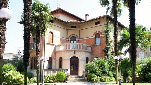 A traditional building with a central entrance, a balcony, and surrounding greenery. - Elegant Art Nouveau Villa With Private Pool Near the Lake (Desenzano del Garda)