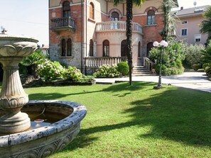 A courtyard with a fountain, a well-maintained lawn, and a building with a balcony and steps leading to the entrance. - Elegant Art Nouveau Villa With Private Pool Near the Lake (Desenzano del Garda)