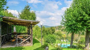 Ein rustikales Holzgebäude mit Strohdach und Steinmauer, im Hintergrund ist ein Schwimmbecken gut sichtbar.