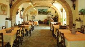 Ein Restaurant mit rustikalem Ambiente, das Backsteinbögen, Steinböden und Holztische und -stühle zeigt.