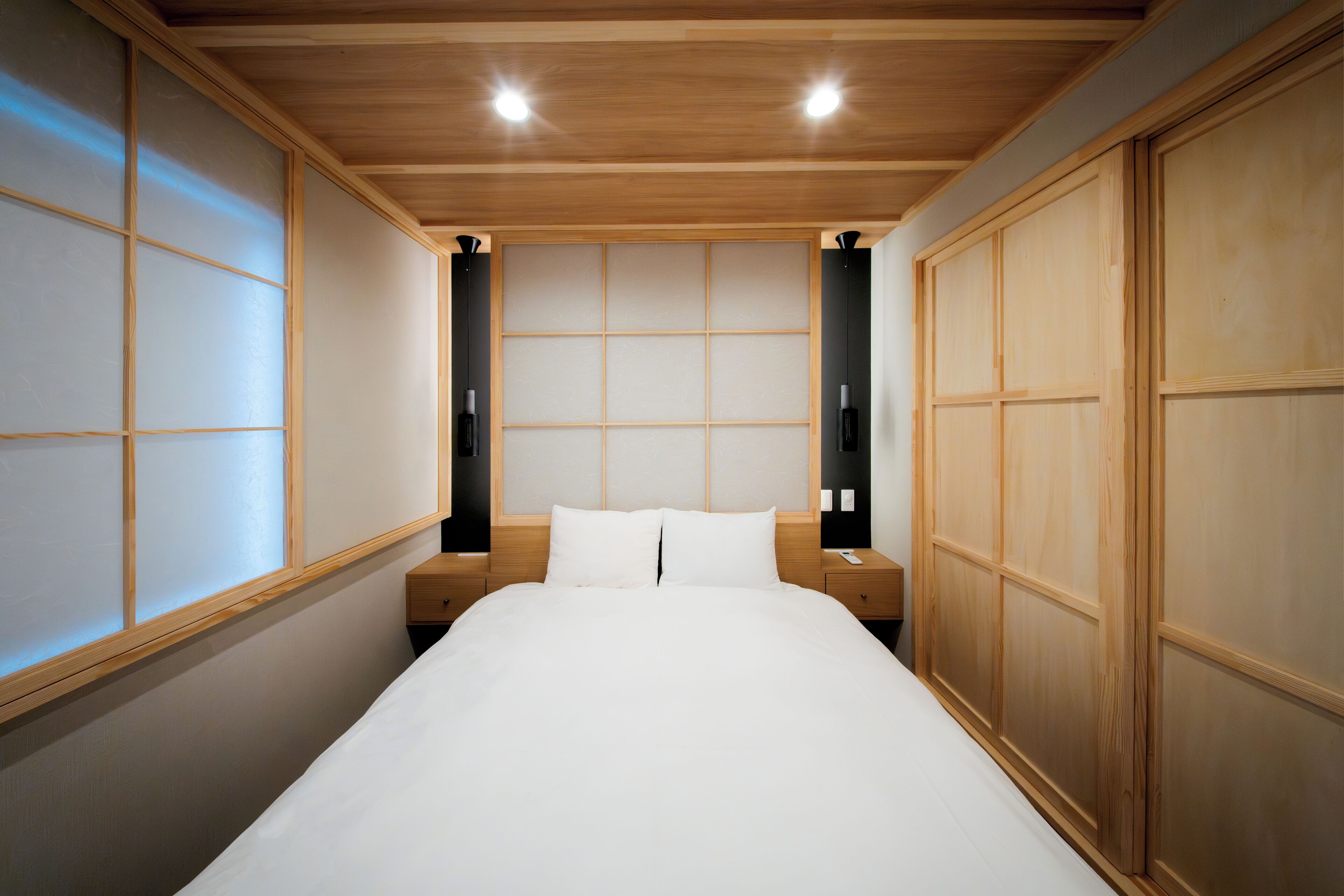 A hotel room with a wooden ceiling, a bed with white bedding, and a traditional Japanese sliding door.