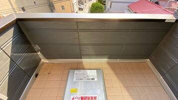 A view from a balcony with a metal grate floor, a metal safety sign, and a red-tiled building in the background.