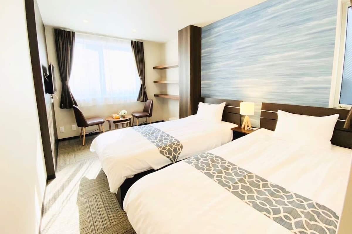 A hotel room with two beds, a desk, a chair, and a view of the sea.