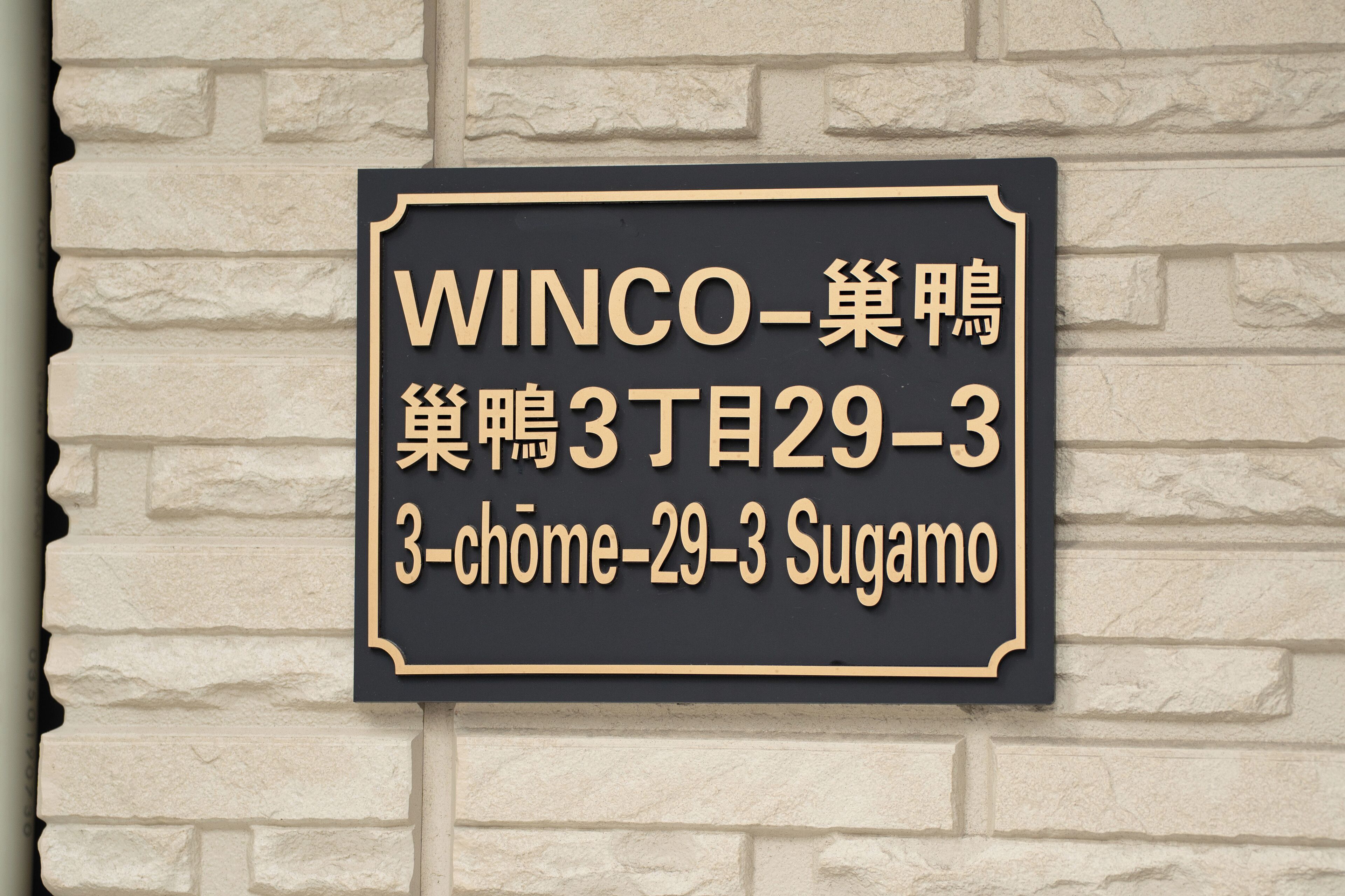 A black and gold sign with white text on a brick wall.