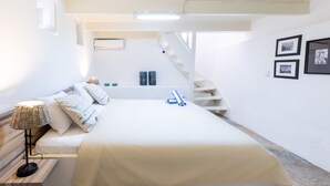 A bedroom with a bed, a nightstand, a lamp, a staircase, and framed pictures on the wall.
