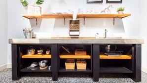 A kitchen with wooden shelves, a countertop, and various kitchen utensils.