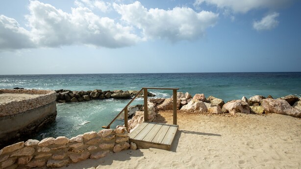 A beach with a wooden deck, stone wall, and rocky shoreline.