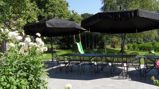 Une terrasse extérieure avec une table et des chaises, entourée de verdure et agrémentée d’une balançoire.