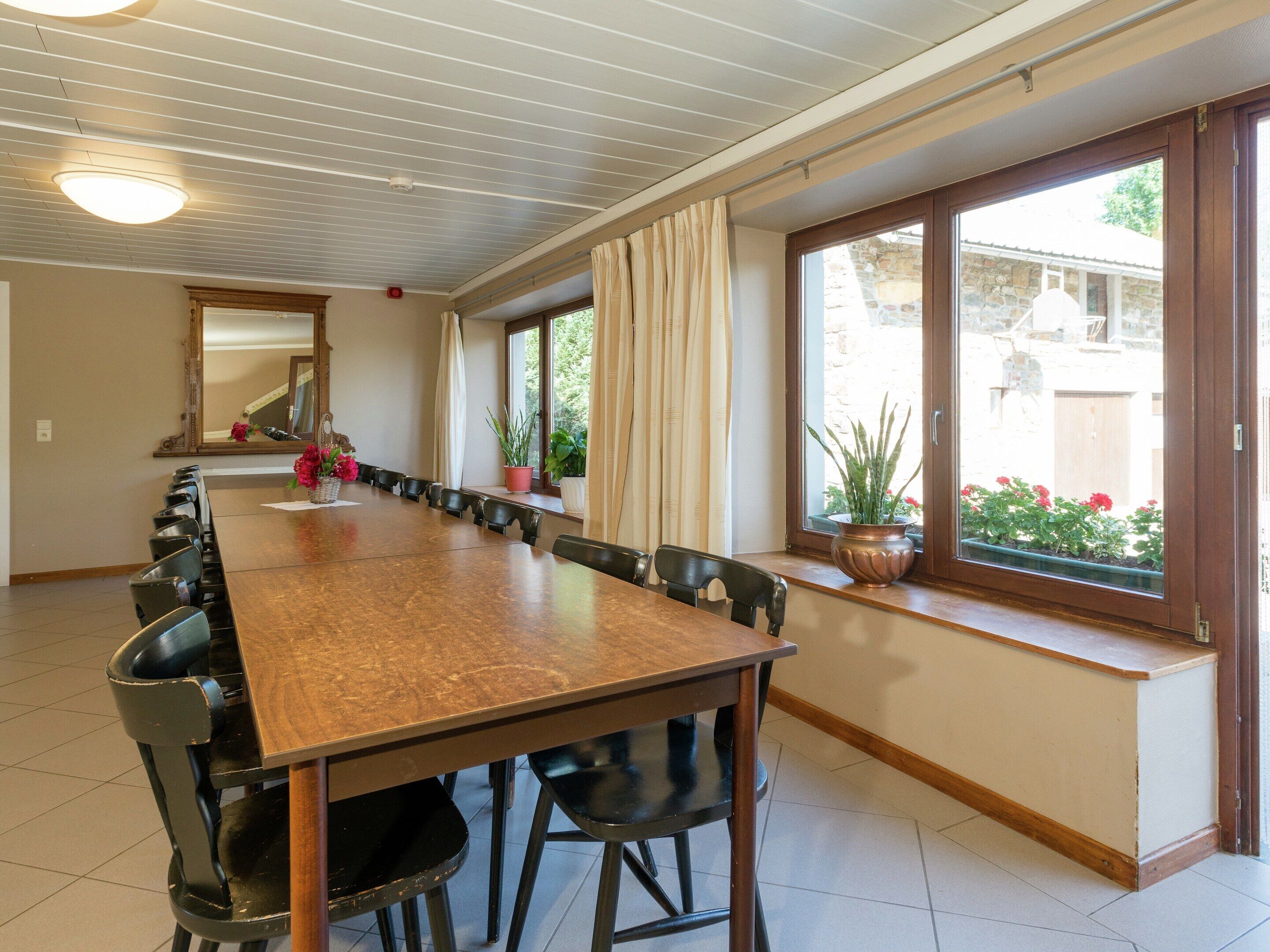 A long dining table with chairs, a mirror, and potted plants.