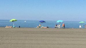 Ein Strand mit mehreren Sonnenschirmen und Menschen, die sich sonnen.