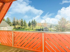 A balcony with a red railing overlooking a grassy area with trees and a small building.