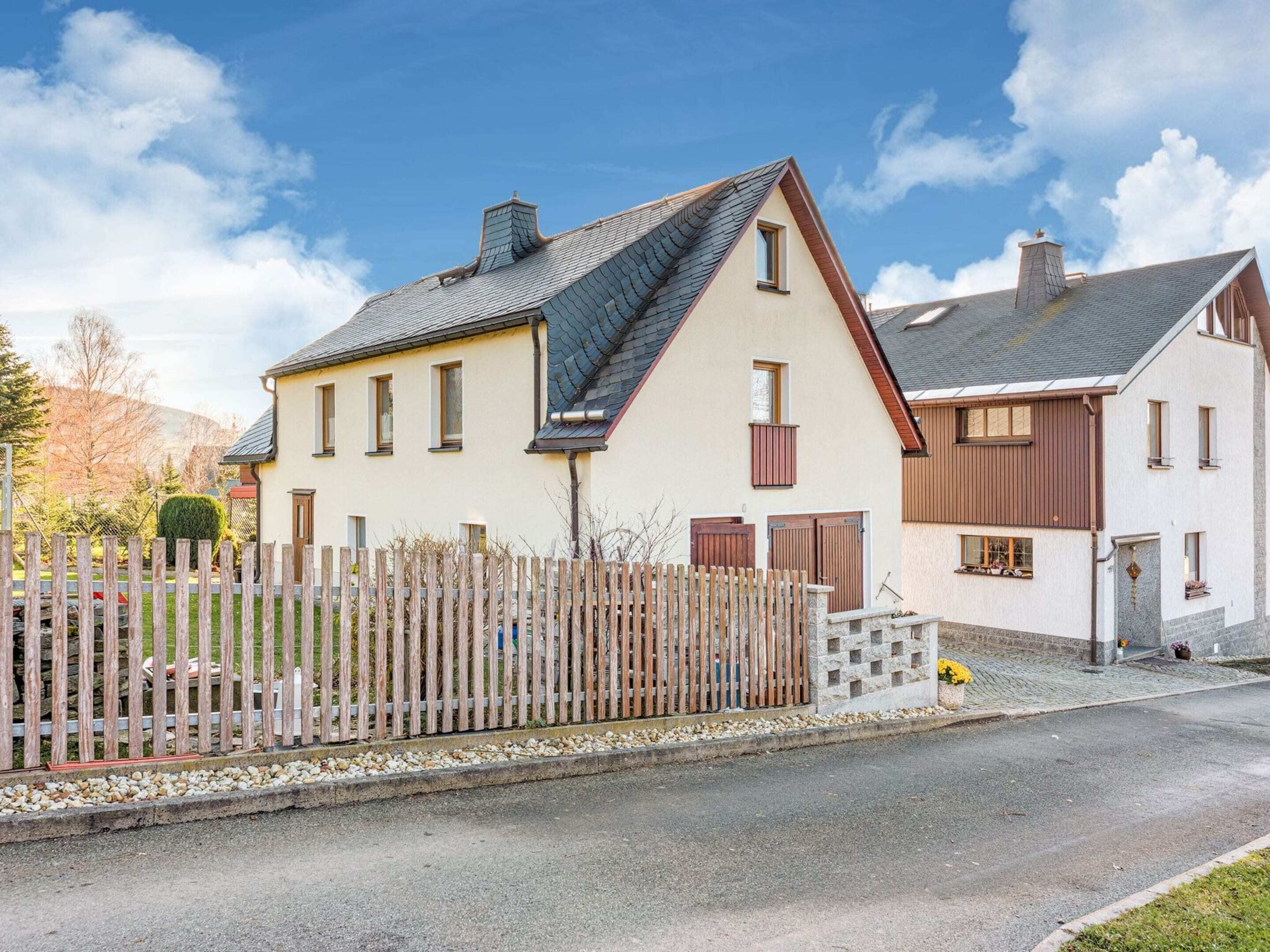 A two-story house with a sloped roof, a wooden fence, and a paved driveway.