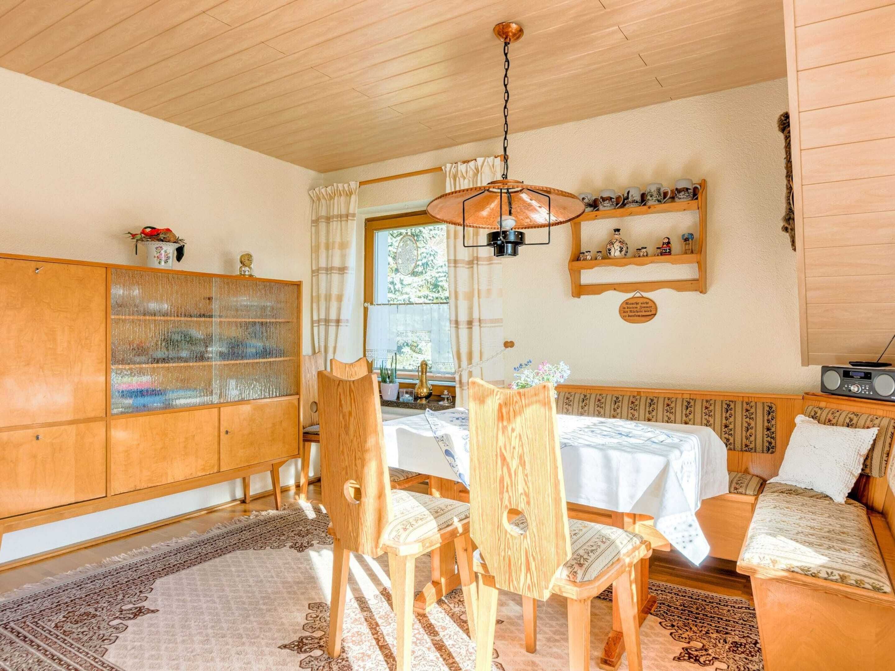 A cozy room with a wooden ceiling, a dining table with chairs, a sofa, a cabinet with glass doors, and a radio on a shelf.