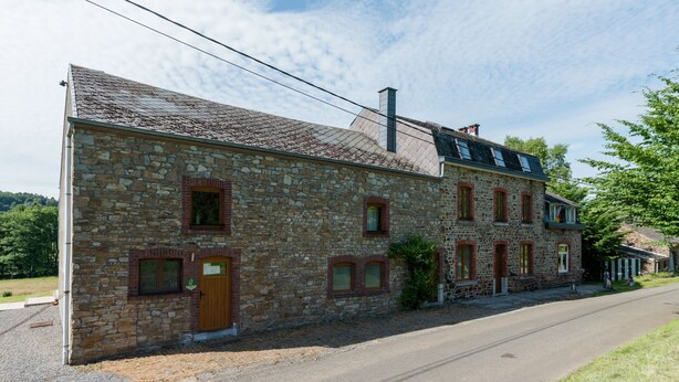 A stone building with a wooden door, multiple windows, and a chimney. - Cottage in Ferrieres With Sauna & Garden (Ferrieres)