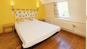A bedroom with a bed, wooden floor, a window with curtains, a radiator, and a wall-mounted light fixture. - Cottage in Ferrieres With Sauna & Garden (Ferrieres)