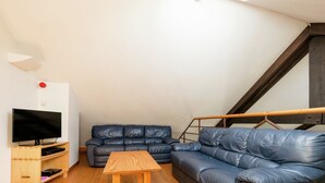 A loft-style living space with a wooden floor, a TV on a wooden stand, a sofa, and a wooden table. - Cottage in Ferrieres With Sauna & Garden (Ferrieres)