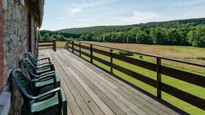 A wooden deck with benches, a stone wall, and a view of a green field and forest. - Cottage in Ferrieres With Sauna & Garden (Ferrieres)