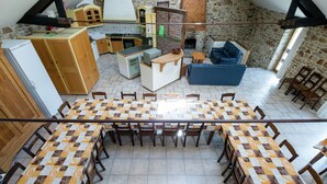 A spacious dining area with a large table and chairs, a kitchen in the background, and a stone wall. - Cottage in Ferrieres With Sauna & Garden (Ferrieres)