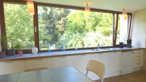 Une cuisine dotée d’une grande fenêtre, de meubles en bois, d’un évier et d’une table à manger avec une chaise.