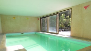 Une grande piscine intérieure aux parois en verre transparent, offrant une vue sur les arbres à l’extérieur.