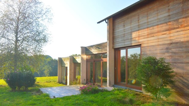 Une maison moderne dotée de grandes fenêtres et d’une façade en bois.