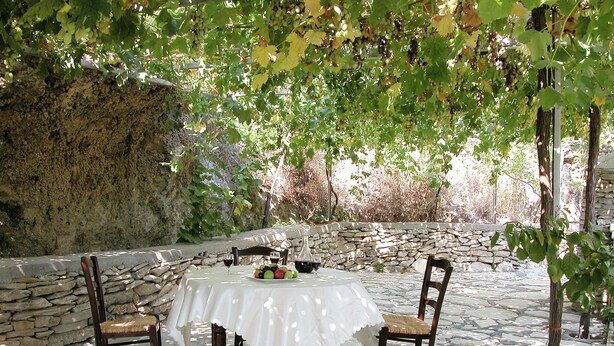 A stone patio with a table and chairs, surrounded by a stone wall and greenery. - Villa in Crete With Private Pool & Views (Heraklion)
