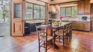 A spacious kitchen with wooden cabinets, a dining table with chairs, and large windows offering a view of the outdoors. - Villa in Crete With Private Pool & Views (Heraklion)