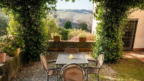 An outdoor seating area with a table and chairs, surrounded by greenery and a view of rolling hills.