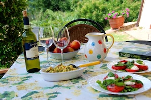 A table set outdoors with a bottle of wine, glasses, a bowl of food, a pitcher, and a book. - Tuscan Haven With Pool (San Casciano in Val di Pesa)