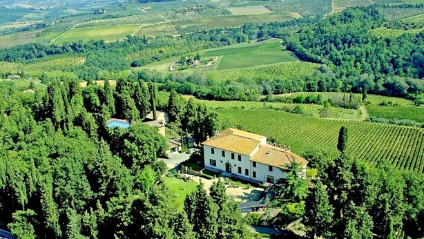 A large, white building with a tiled roof surrounded by vineyards and greenery.