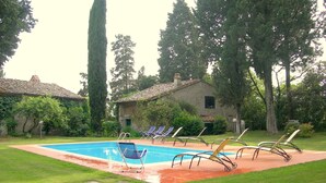 A swimming pool with lounge chairs, surrounded by grass and trees.