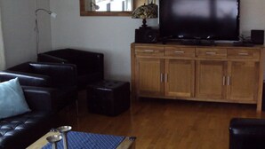 A living room with a black leather sofa, a wooden cabinet with a television on top, and a floor lamp. - Detached House With Sauna Near Ski Lifts (Winterberg)