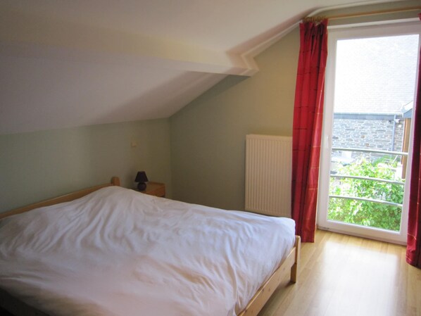 A bedroom with a bed, a nightstand, a lamp, a radiator, and a window with curtains.