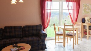 A cozy living room with a plaid sofa, a wooden coffee table, and a dining area with a table and chairs. - Chic Vacation Home near Forest in Sebnitz Germany (Sebnitz)