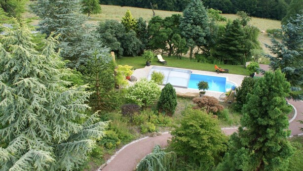 A residential area with a swimming pool surrounded by trees and a paved path. - Chic Vacation Home near Forest in Sebnitz Germany (Sebnitz)