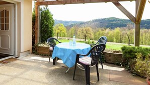 A covered patio with a table and chairs, overlooking a scenic landscape with trees and hills. - Chic Vacation Home near Forest in Sebnitz Germany (Sebnitz)